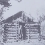 Enos Mills at a cabin doorway on Longs Peak, photographed before 1922.