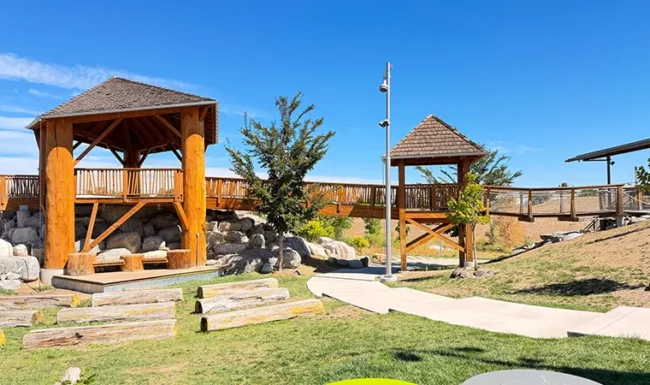 Nature playground with wooden play structures, boulders and log seating at Westminster Station Park