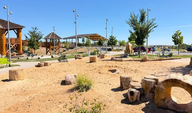 Sand play area with tree stumps and hollow log at Westminster Station Park Nature Playground