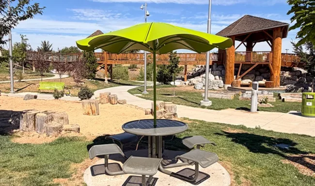 Shaded picnic table with wooden nature playground in the background at Westminster Station Park