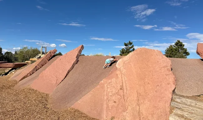 Child climbing natural boulders at McKay Lake Park’s nature playground in Broomfield