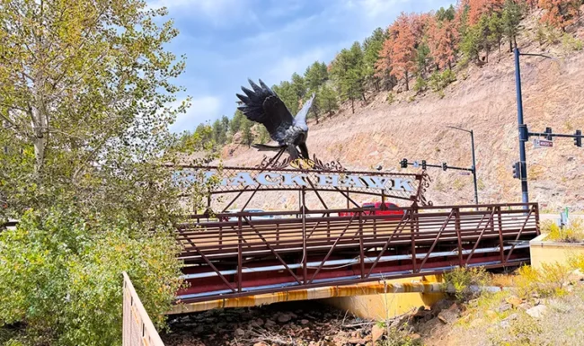 Bronze black hawk sculpture above a pedestrian bridge over North Clear Creek in Black Hawk, Colorado