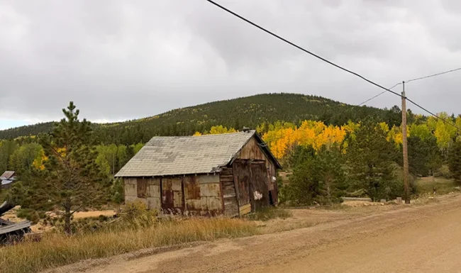 Weathered mining shack beside a dirt road and golden aspens near Central City, Colorado