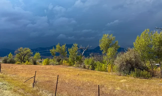 Open grassland and foothills beneath dramatic storm clouds
