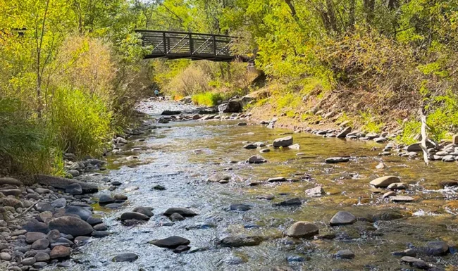 St. Vrain Creek flowing through Bohn Park with rocks and a pedestrian bridge