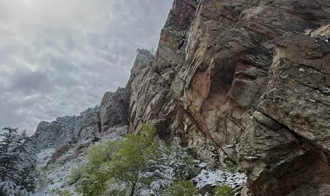 Towering sandstone cliff above snow-covered trees in Eldorado Canyon