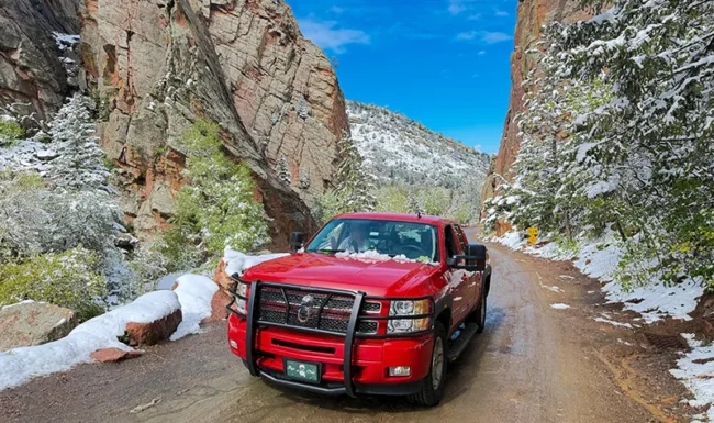 Fred's red pickup parked beneath snowy sandstone cliffs in Eldorado Canyon