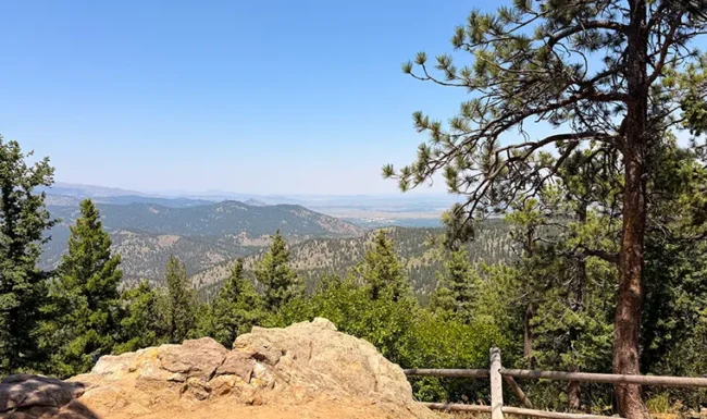 Mountain scenery from Lost Gulch Overlook, framed by pine trees, rocks and a wooden railing