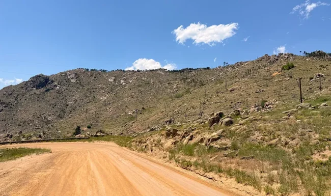 Unpaved Sunshine Canyon Drive curving beneath a rocky, sparsely wooded hillside on the way to Gold Hill, Colorado.
