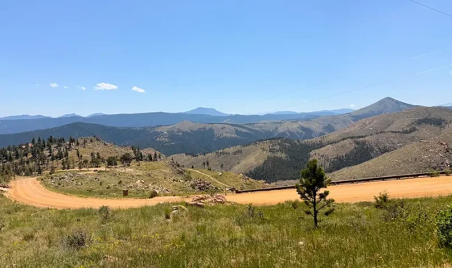 Sunshine Canyon Drive winding past grassy slopes with sweeping mountain views on the way to Gold Hill, Colorado.