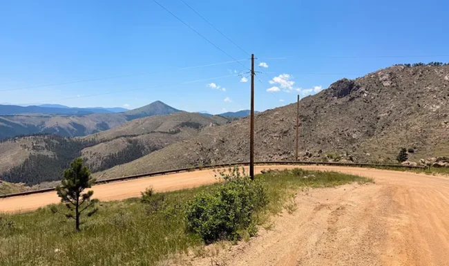 Sharp bend on unpaved Sunshine Canyon Drive overlooking rugged hills and forested valleys near Gold Hill, Colorado.