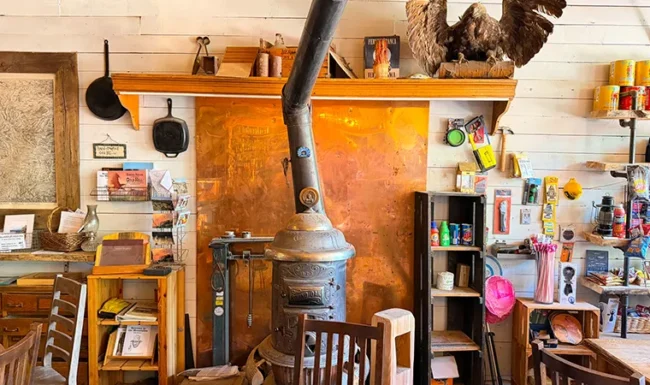 An ornate potbelly stove surrounded by cast-iron pans, books, and rustic decor inside Gold Hill General Store.