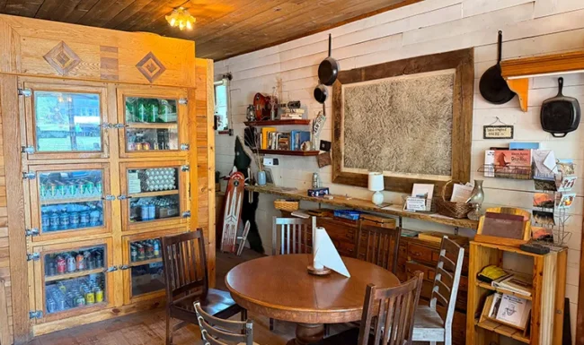Wooden table and chairs beside a beverage cooler and framed wall map inside Gold Hill General Store.