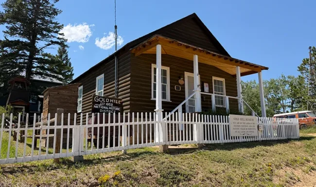 Gold Hill Museum log building with a covered front porch and white picket fence.