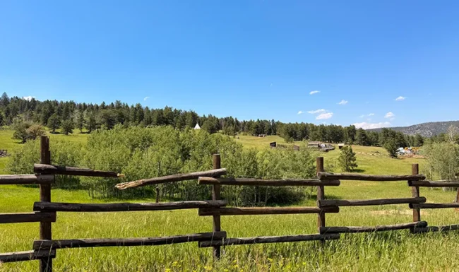 Distant white teepee beyond a green meadow and rustic wooden fence at The Colorado Mountain Ranch near Gold Hill, Colorado.