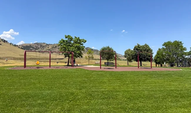 Playground swings and open grassy field at Foothills Community Park in Boulder Colorado
