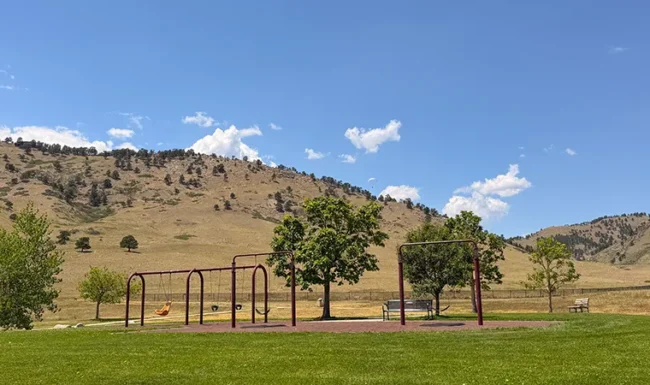 Playground swings with foothill views and paraglider overhead at Foothills Community Park in Boulder Colorado