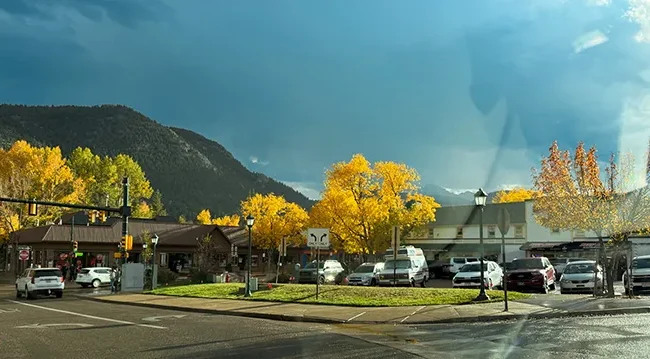 Downtown Estes Park storefronts beneath storm clouds and golden aspen and fall trees
